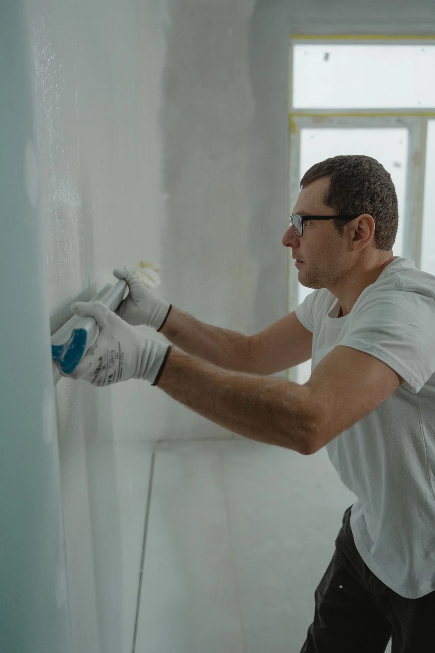 Technician smoothing fresh drywall compound on an interior wall