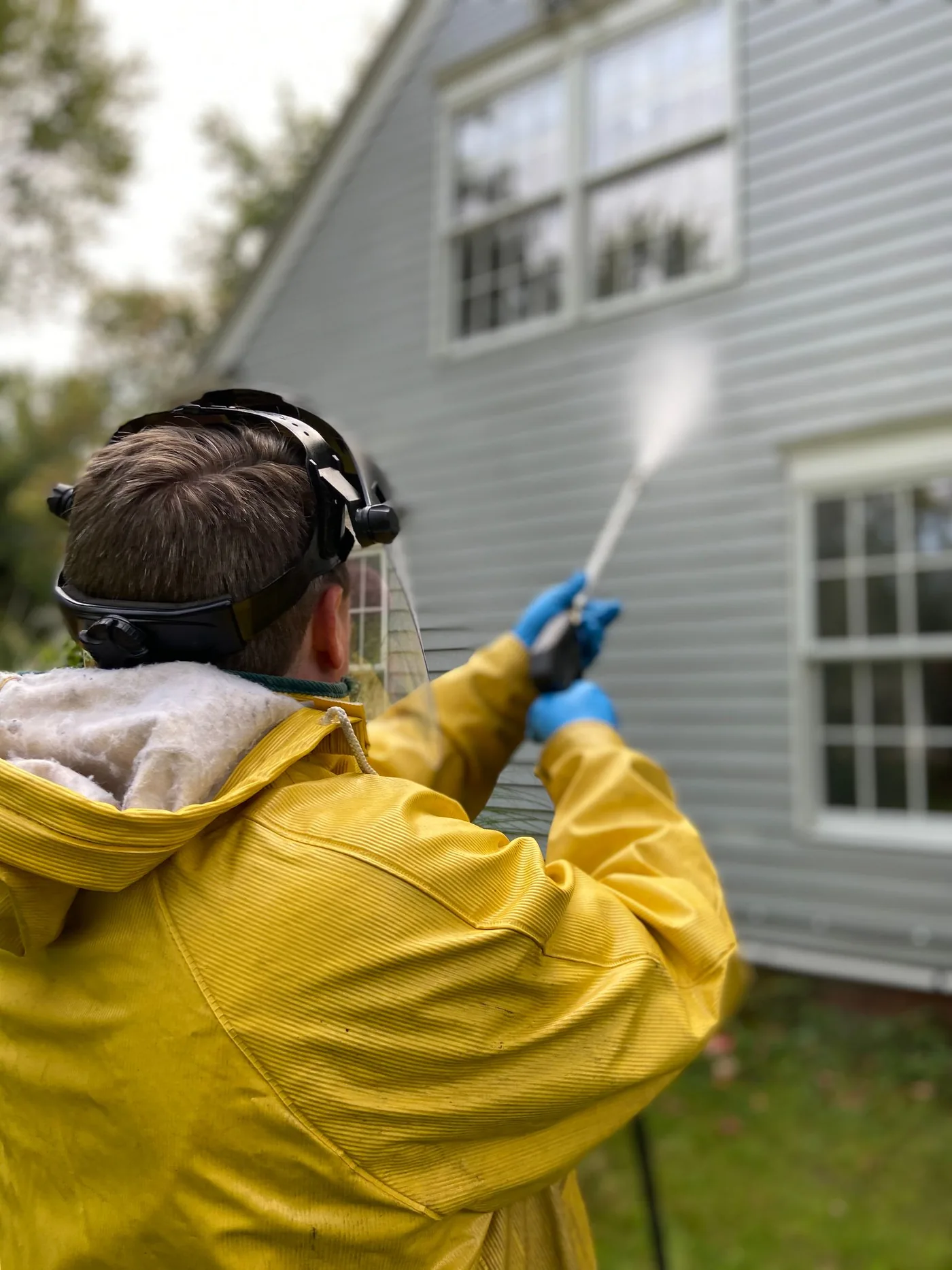 Technician pressure washing the siding of a home back to a clean finish